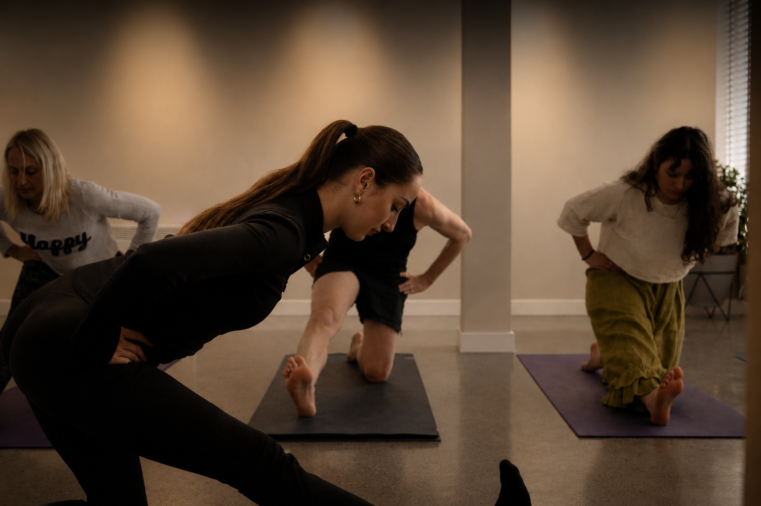 Pilates class practicing half split stretch pose in a warm and calming indoor wellness studio.