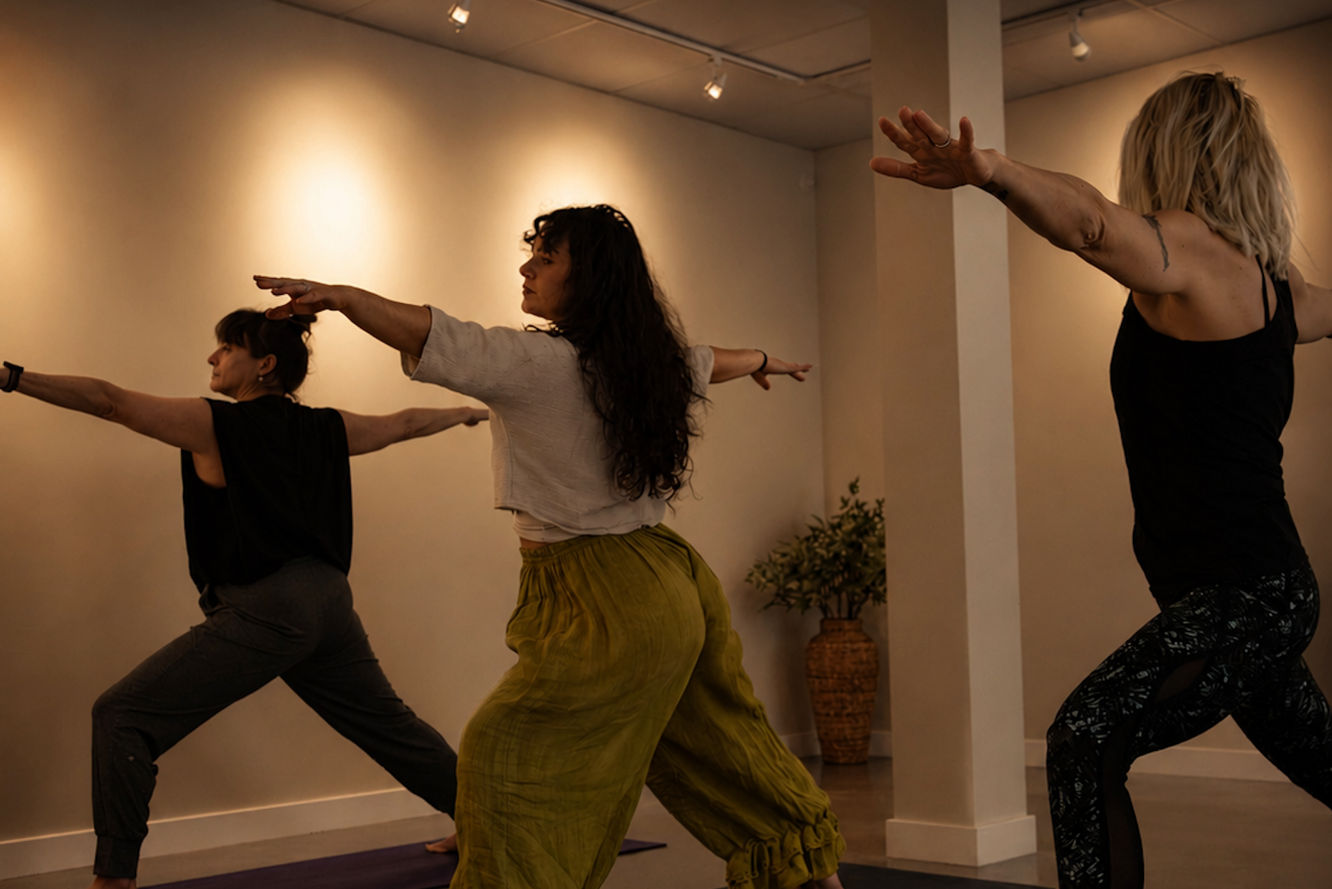 Women practicing Warrior II yoga pose in a warm and calming indoor yoga studio.